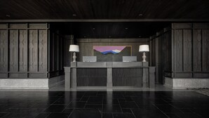 Balcão de recepção com duas luminárias, um quadro e decoração em madeira escura.