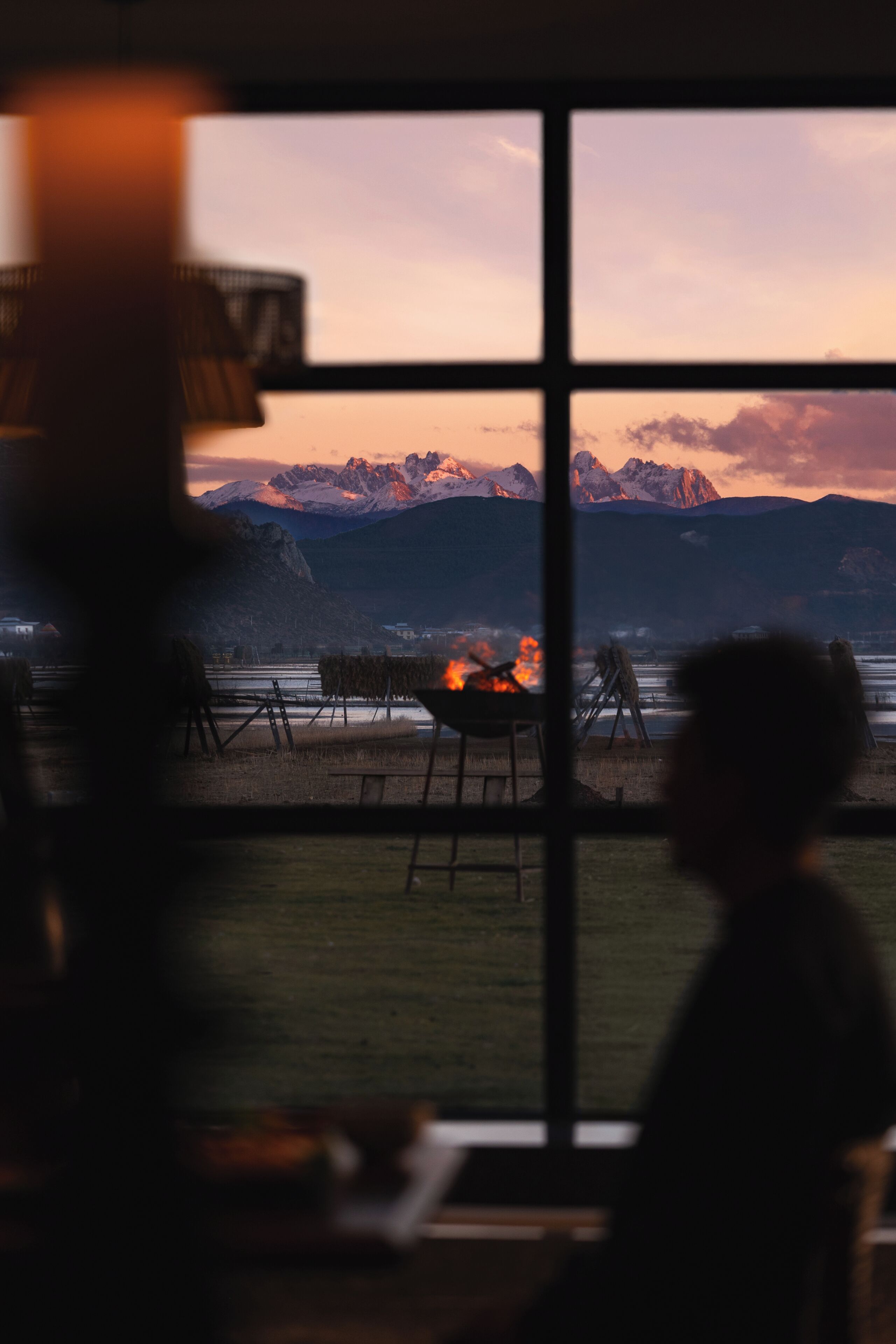 Blick durch ein Fenster auf ein Feuer, Berge und einen Stuhl.