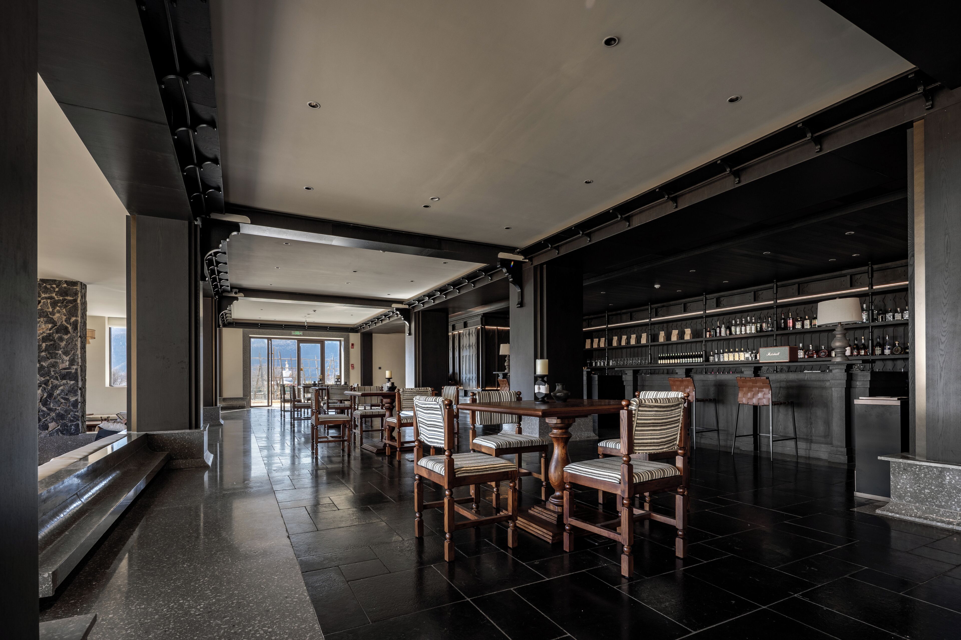 A spacious hotel lobby with a bar area, wooden chairs, and a stone wall.