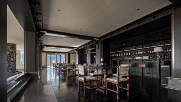 A spacious hotel lobby with a bar area, wooden chairs, and a stone wall.