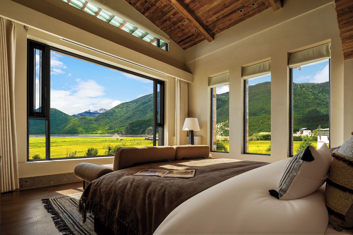 Un dormitorio con ventanas amplias, una cama, una mesita de noche y vistas a un paisaje verde.