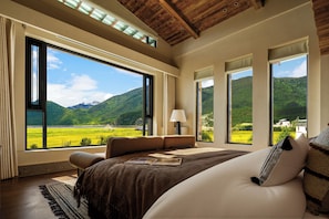 Un dormitorio con ventanas amplias, una cama, una mesita de noche y vistas a un paisaje verde.
