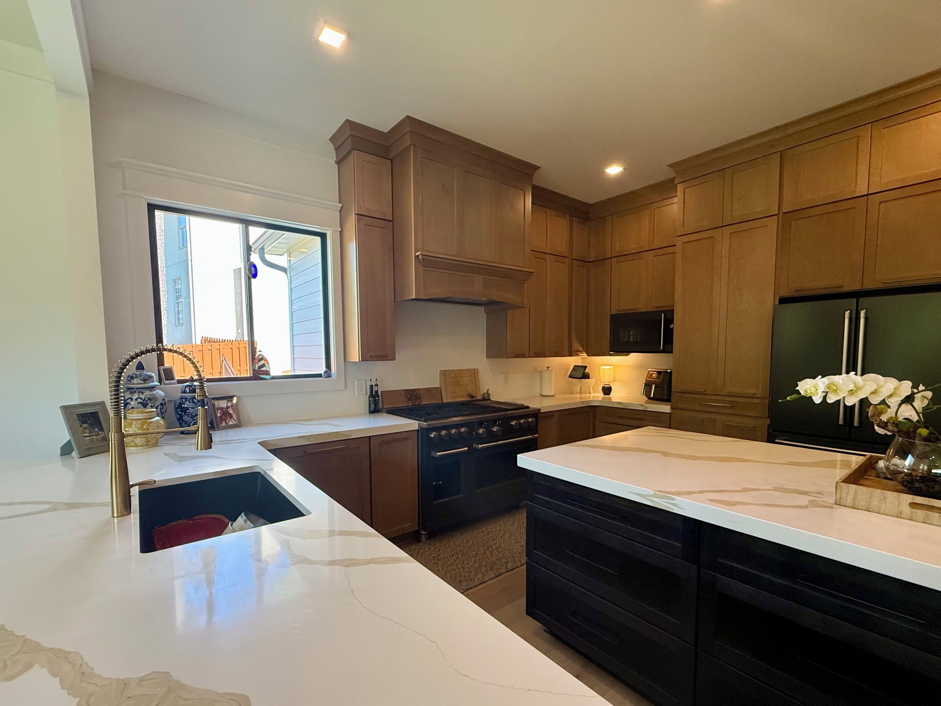 A modern kitchen with wooden cabinets, a stainless steel refrigerator, and a marble countertop.