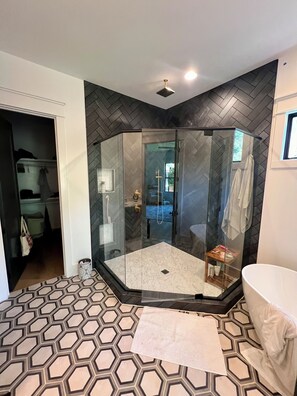 Un bagno moderno con doccia vetrata, una vasca da bagno bianca e un pavimento a motivi.
