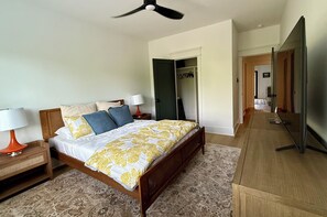 Un dormitorio con una cama, dos mesitas de noche, un ventilador de techo, un armario y un espejo.
