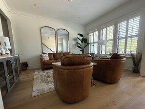 Una sala de estar con sofá, sillones, una mesa de centro, alfombra, aparador y un espejo grande.