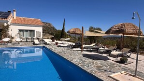 A swimming pool with lounge chairs and umbrellas, a building with a tiled roof, and a clear sky.