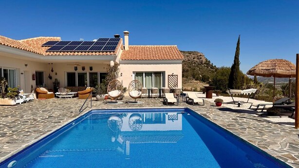 Zona de piscina amb una piscina blava cristal·lina, gandules i un edifici amb teulada d'estuc.
