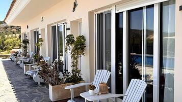 A hotel exterior with a row of sun loungers, potted plants, and a stone-paved walkway.