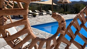 Zona de piscina amb una estructura de latici de fusta, gandules i un cel blau clar.