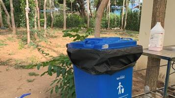 Ein blauer Mülleimer mit Recycling-Symbol, ein blauer Gartenschlauch und ein Tisch mit einem weißen Behälter.