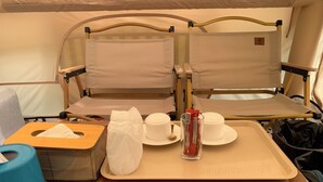 Un espacio habitable reducido con una cama, una mesita con una bandeja que contiene un pañuelo, una taza, una botella y una bolsa.