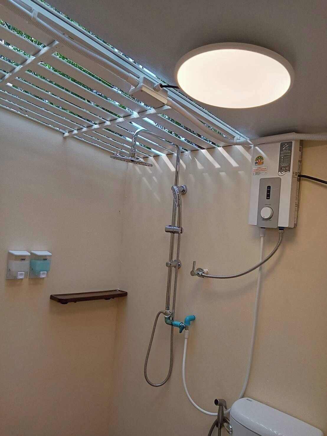 Ein Duschbereich mit einer Deckenleuchte, einer Handbrause und einem an der Wand montierten Bedienfeld.