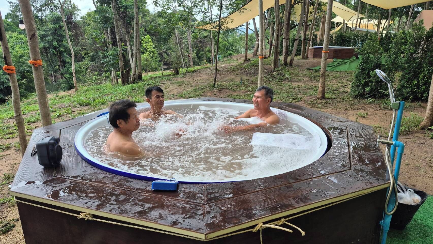 A hot tub with three people in it, surrounded by trees and a covered area.