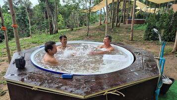 A hot tub with three people in it, surrounded by trees and a covered area.