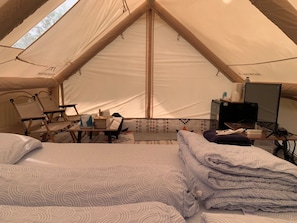 Un hébergement sous tente comprenant un lit, des chaises, une table et un bureau avec un ordinateur.