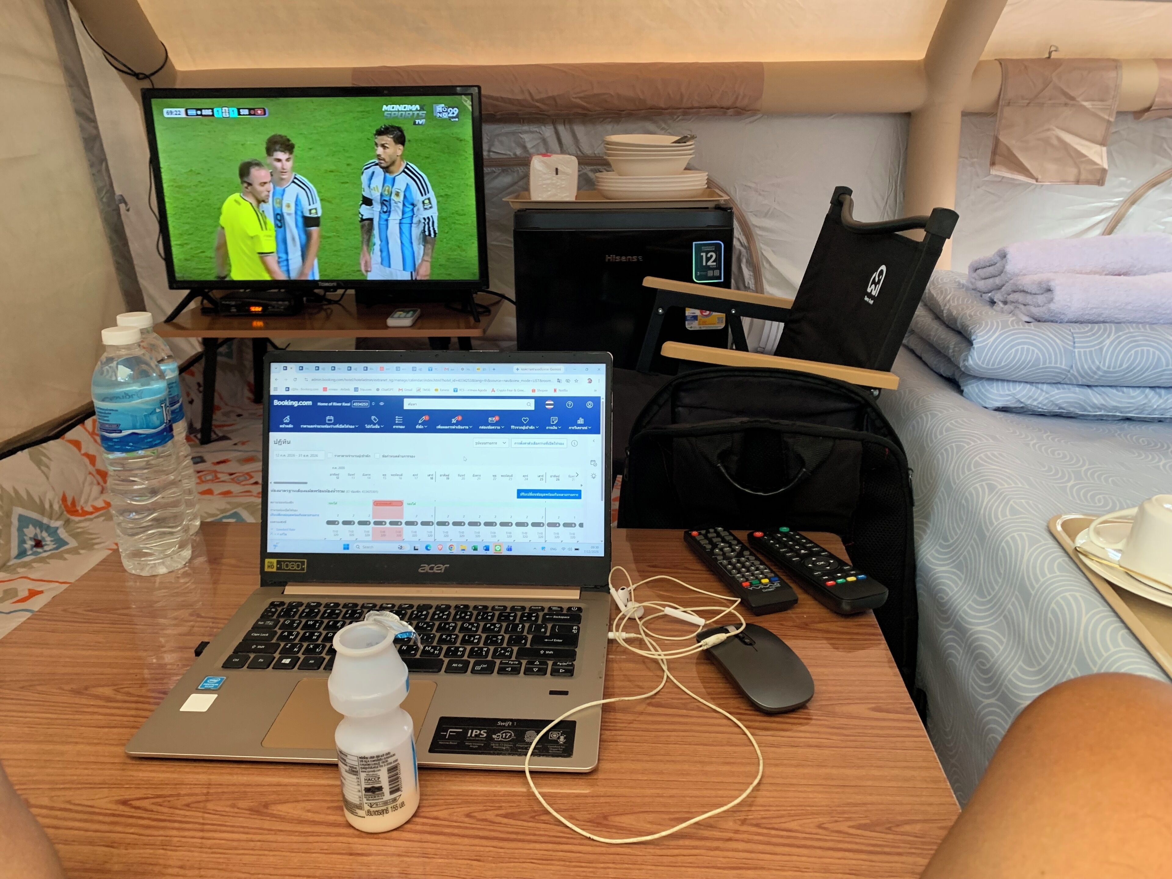 A hotel room with a laptop, a bottle of water, a remote control, and a bed with a blanket.