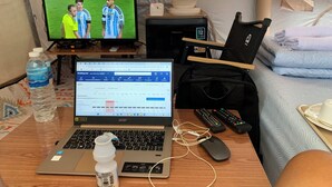 Una habitación de hotel con una computadora portátil, una botella de agua, un control remoto y una cama con una manta.