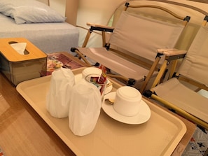Un plateau bien rangé, sur lequel on trouve une boîte de mouchoirs, une tasse et un petit récipient, probablement destiné aux articles de toilette, est posé sur une table en bois dans une chambre d’hôtel.