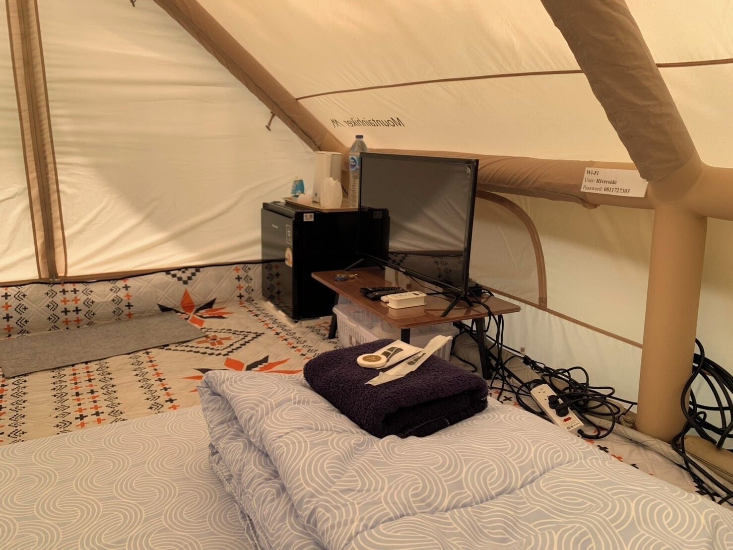 A tent with a bed, a small table with a computer, and a power outlet.