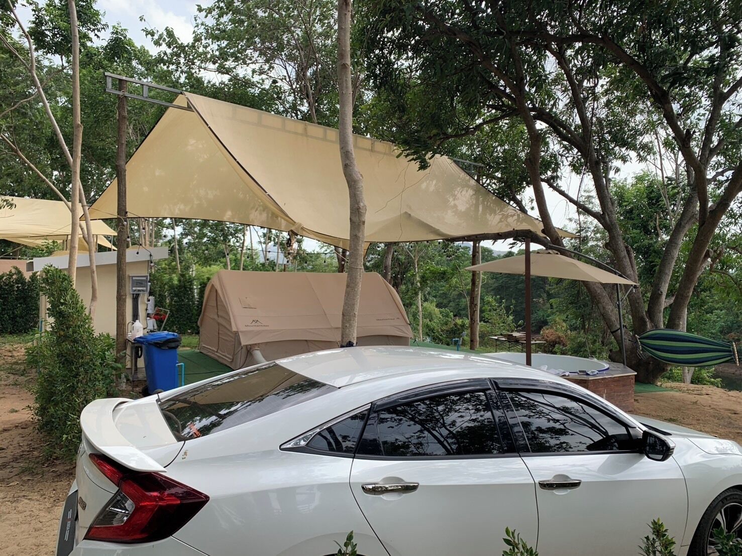 A white car parked in a campsite with a tent and a canopy.