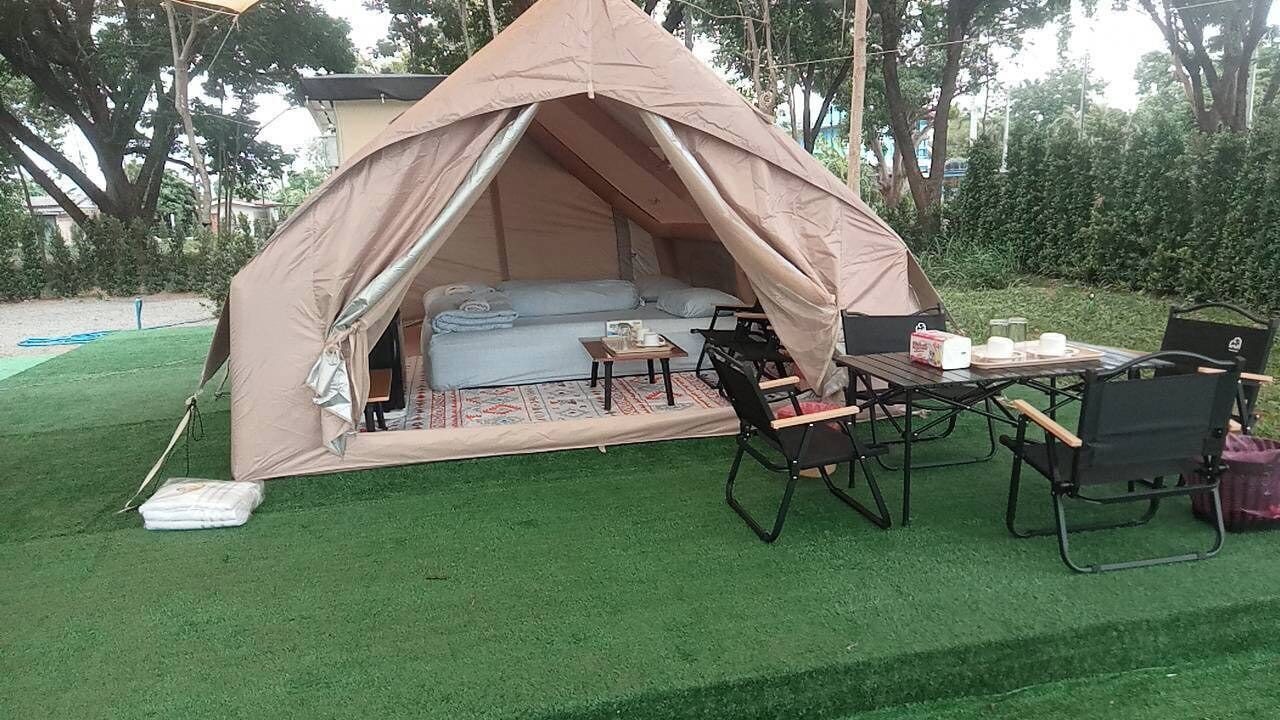 A tent with a sofa and table set up on artificial grass, surrounded by trees.