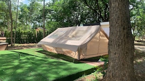 A tent set up in a wooded area with a green artificial turf surface. - Riverside Glamping Resort Kanchanaburi (Kanchanaburi)