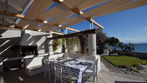 An outdoor patio with a table set for dining, a grill, and a view of the sea.