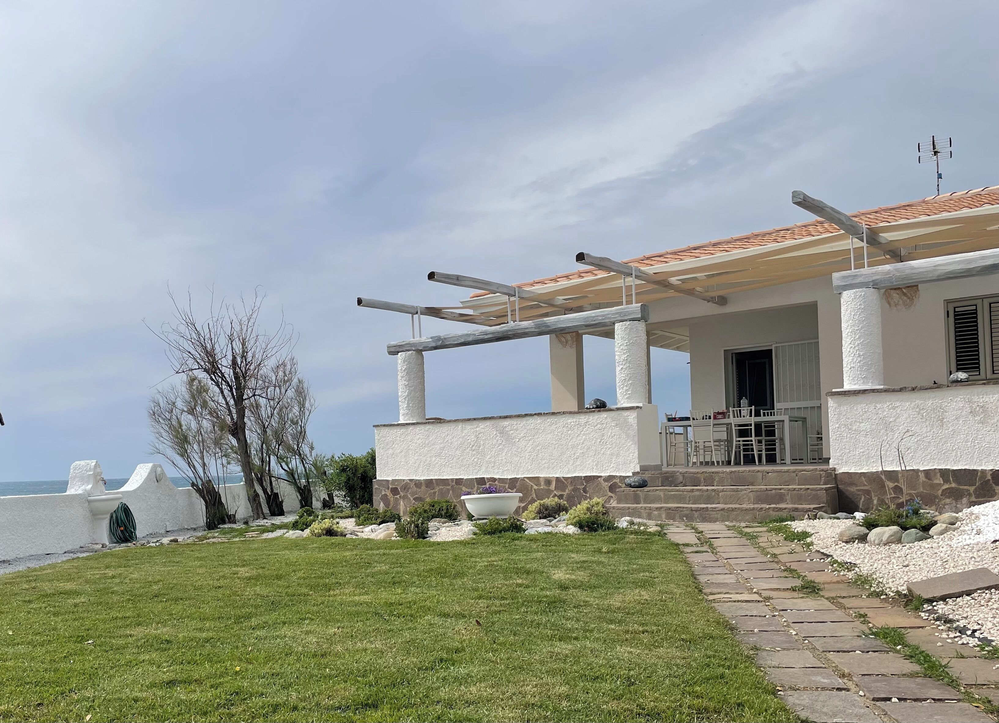 Ein Küstenhaus mit überdachter Terrasse, Steinmauern und Meerblick.