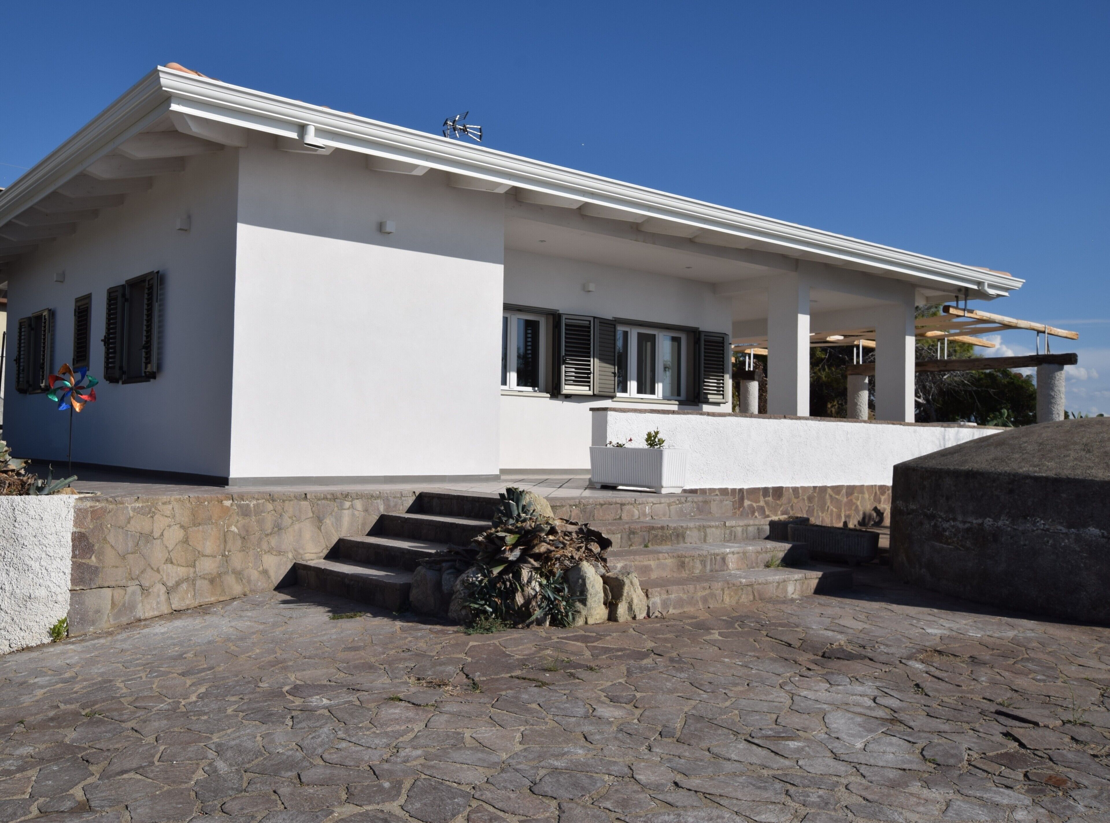 A modern house with a stone staircase leading to a white door, a small garden area, and a clear blue sky.