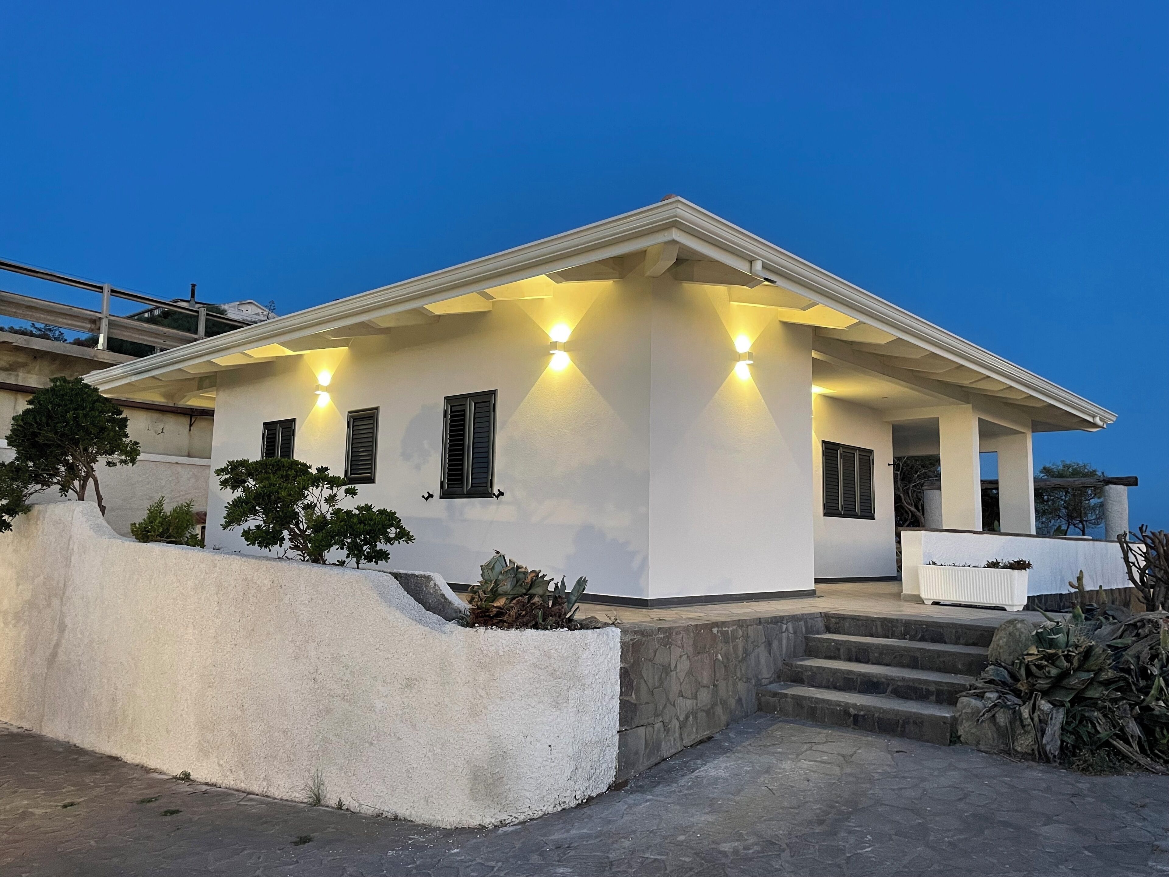 A modern house with a white exterior, a covered porch, and a stone retaining wall.