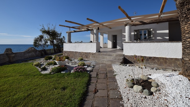 A coastal property with a stone pathway leading to a wooden deck overlooking the sea.