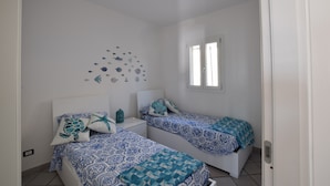 A bedroom with two beds, a white ceiling, a wall decoration of sea creatures, and a window.