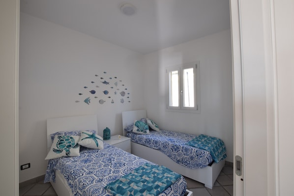 A bedroom with two beds, a white ceiling, a wall decoration of sea creatures, and a window.