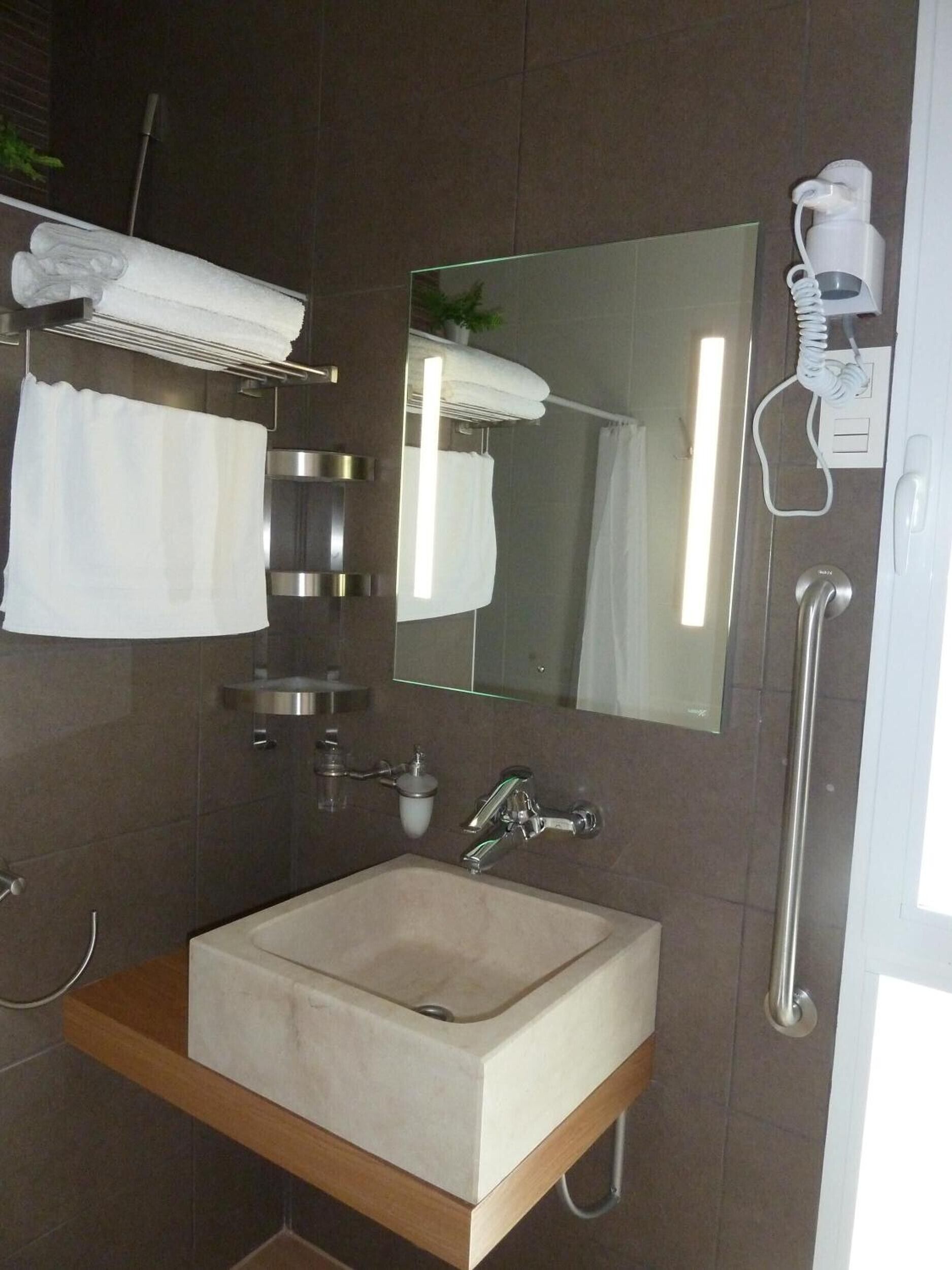 A modern bathroom with a built-in sink, a towel rack, a mirror, and a hand dryer.