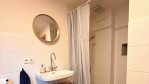 Une salle de bain équipée d’un lavabo, d’un miroir, d’un porte-serviettes, d’un rideau de douche et d’un petit meuble de rangement.
