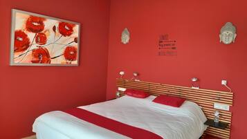 A bedroom with a bed, red walls, a painting, and two Buddha statues.