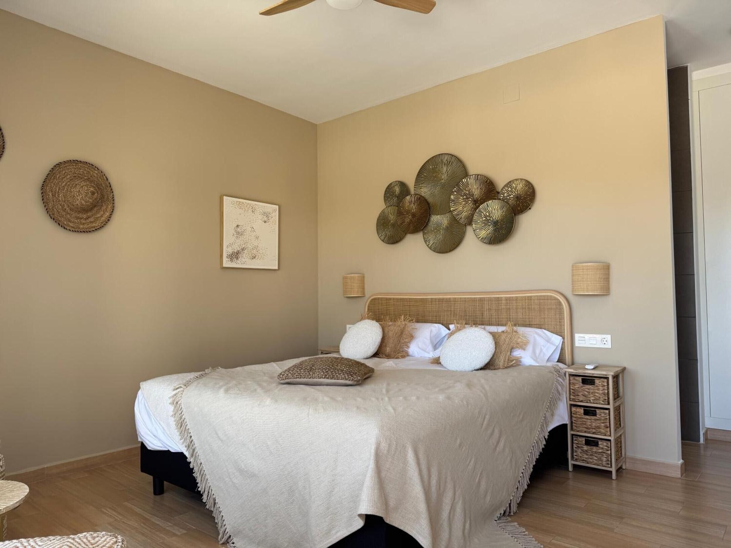 Un dormitorio con cama, lámparas de noche, un adorno en la pared y una cesta tejida.