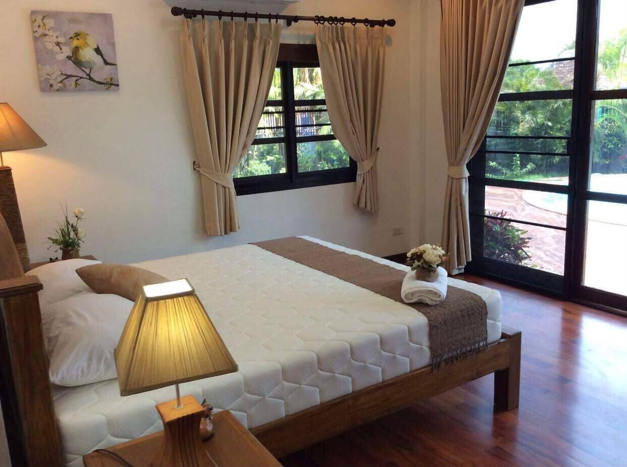 A bedroom with a bed, a bedside lamp, a window with curtains, and a painting on the wall.