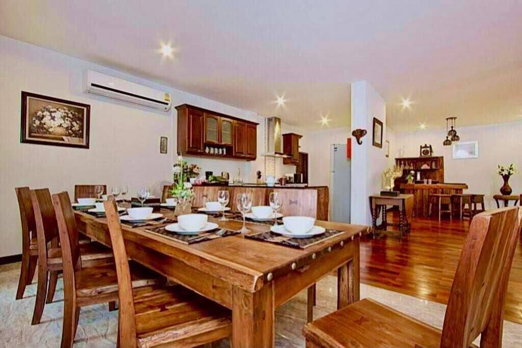 A dining area with a wooden table set for four, flanked by wooden chairs, a kitchen in the background, and a living area with a sofa and coffee table.