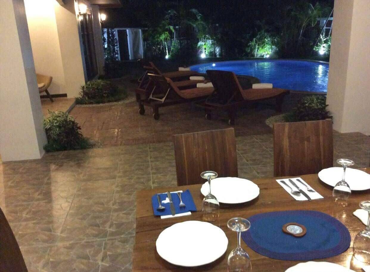 Un coin repas avec vue sur la piscine, comprenant une table dressée pour deux personnes, avec assiettes, couverts et verres.