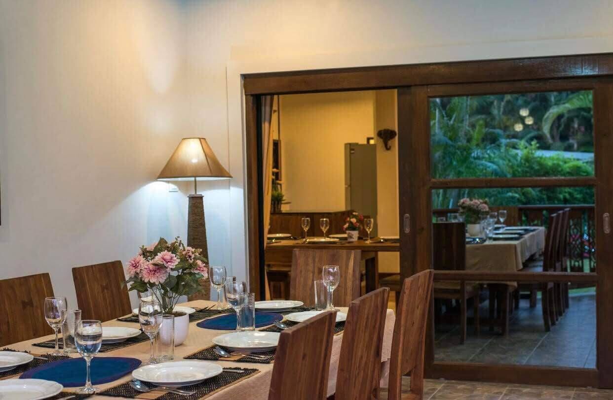 A dining area with a table set for four, a lamp, and a view through a glass door to an outdoor dining space.