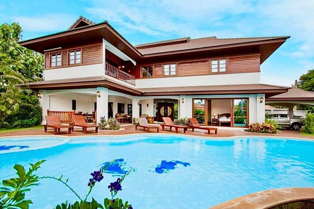 Una casa de dos pisos con piscina, mobiliario exterior y un balcón.