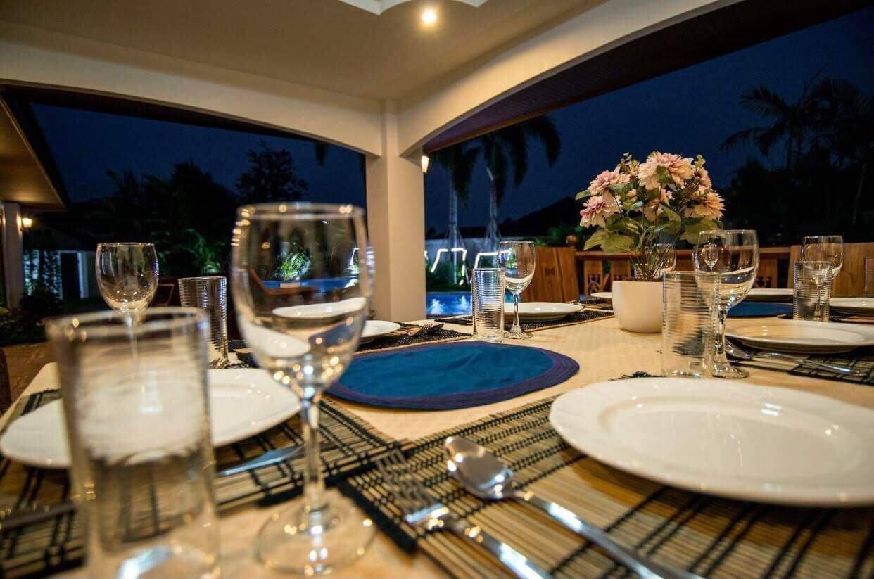 A dining table set for a meal with plates, glasses, and cutlery, overlooking a pool area.