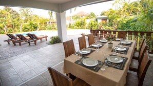 An outdoor dining area with a table set for four, surrounded by chairs, and a pool with lounge chairs in the background. - Oriental Thai Luxury Villa With Private Pool, Chiangmai, Thailand (Tambon San Phi Suea)
