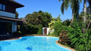 A swimming pool with a curved edge, surrounded by lush greenery and a house with a visible door. - Oriental Thai Luxury Villa With Private Pool, Chiangmai, Thailand (Tambon San Phi Suea)