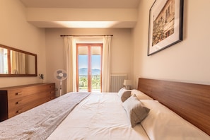 A hotel room with a bed, a dresser, a fan, a window with curtains, and a framed picture on the wall.