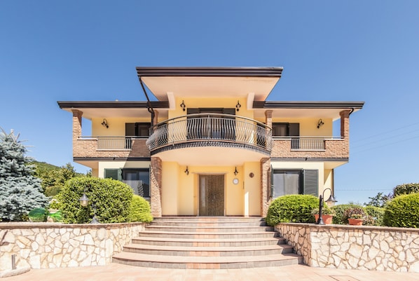 A two-story house with a central balcony, stone walls, and a tiled entrance.