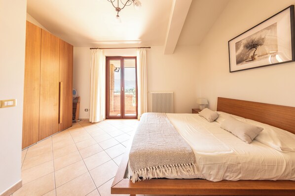 A bedroom with a large bed, a wooden wardrobe, a radiator, and a view through a glass door.