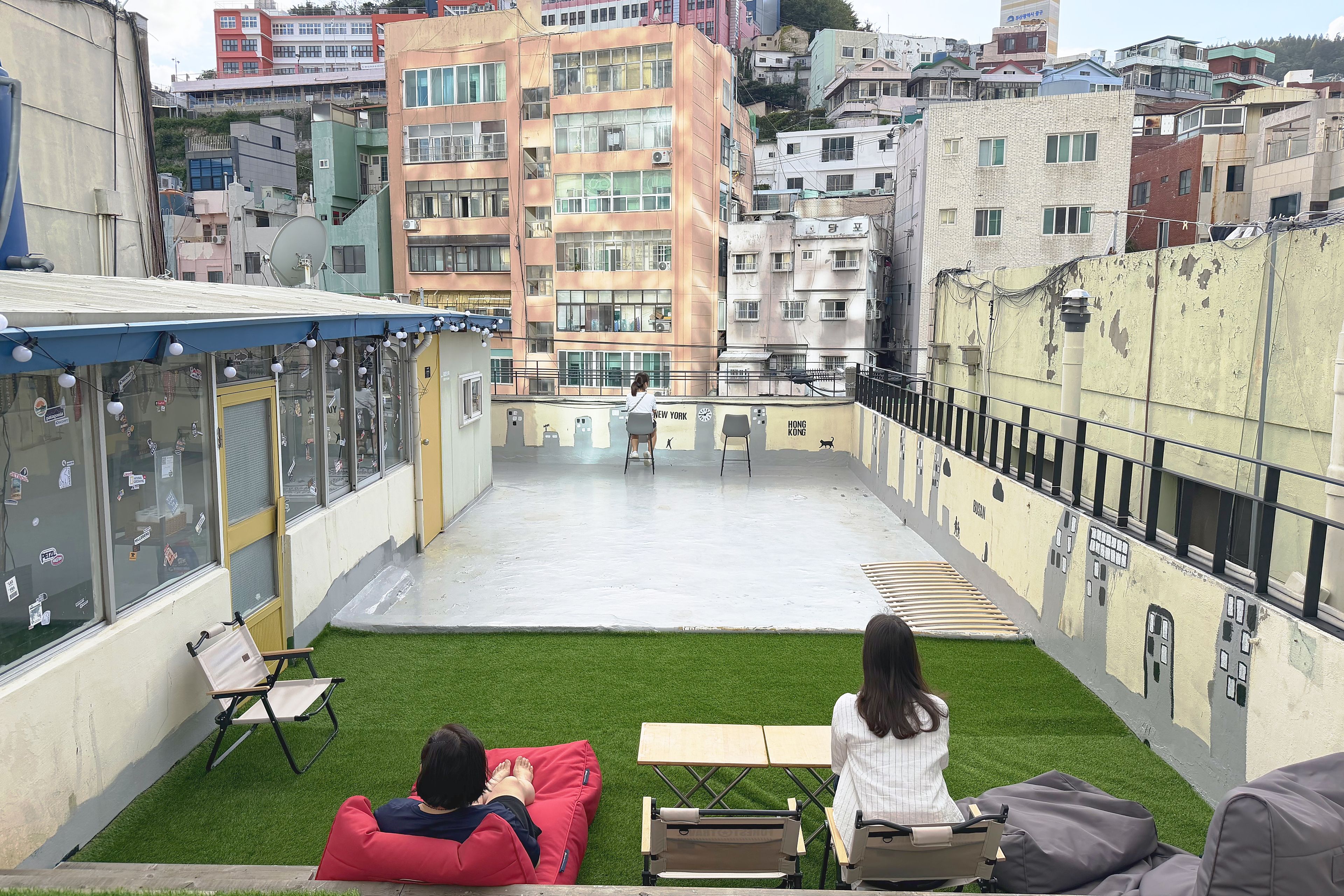 A rooftop terrace with a view of a cityscape, a small patch of artificial grass, and a few seating areas.